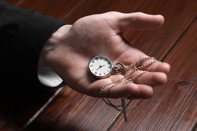 Photo of Man holding chain with elegant pocket watch at wooden table, closeup