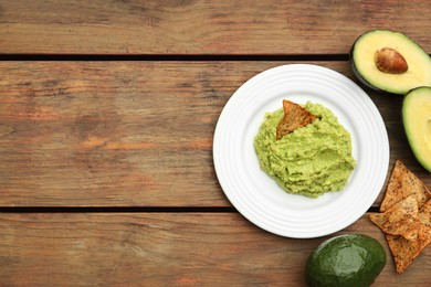 Photo of Delicious guacamole, avocado and nachos on wooden table, flat lay. Space for text
