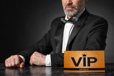 Photo of Man sitting at table with VIP sign on black background, closeup