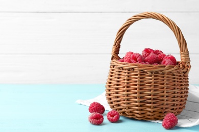 Photo of Basket of delicious fresh ripe raspberries on blue wooden table against white background, space for text