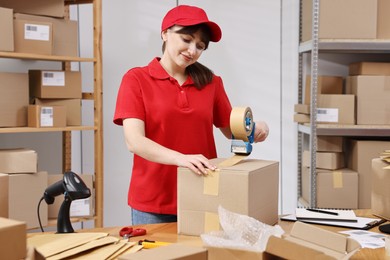 Photo of Parcel packing. Post office worker taping box at wooden table indoors