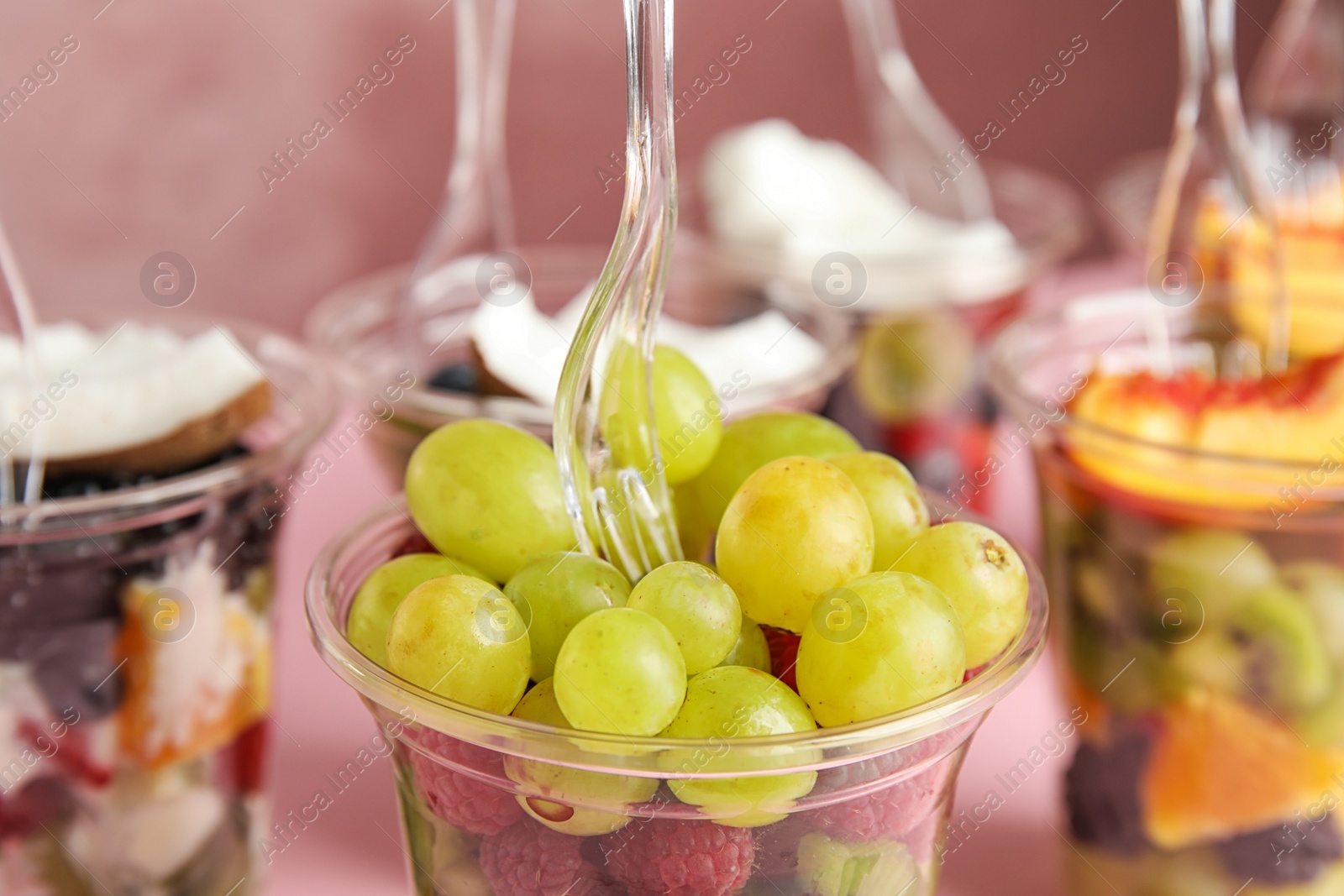 Photo of Fresh tasty fruit salad in plastic cups on pink background, closeup