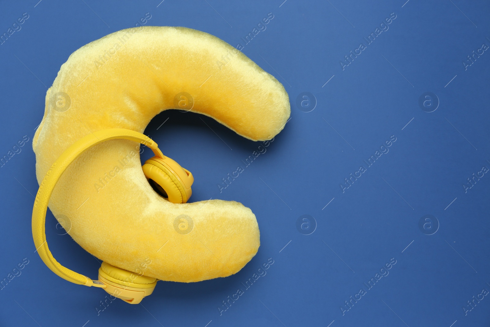 Photo of Yellow travel pillow and headphones on blue background, top view. Space for text