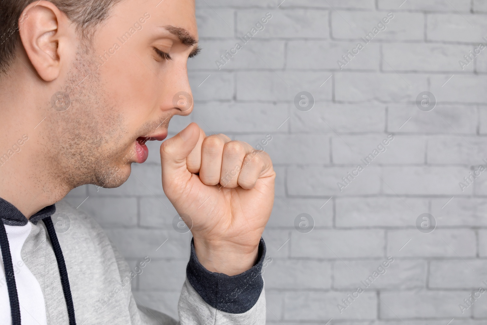 Photo of Young man coughing on brick wall background