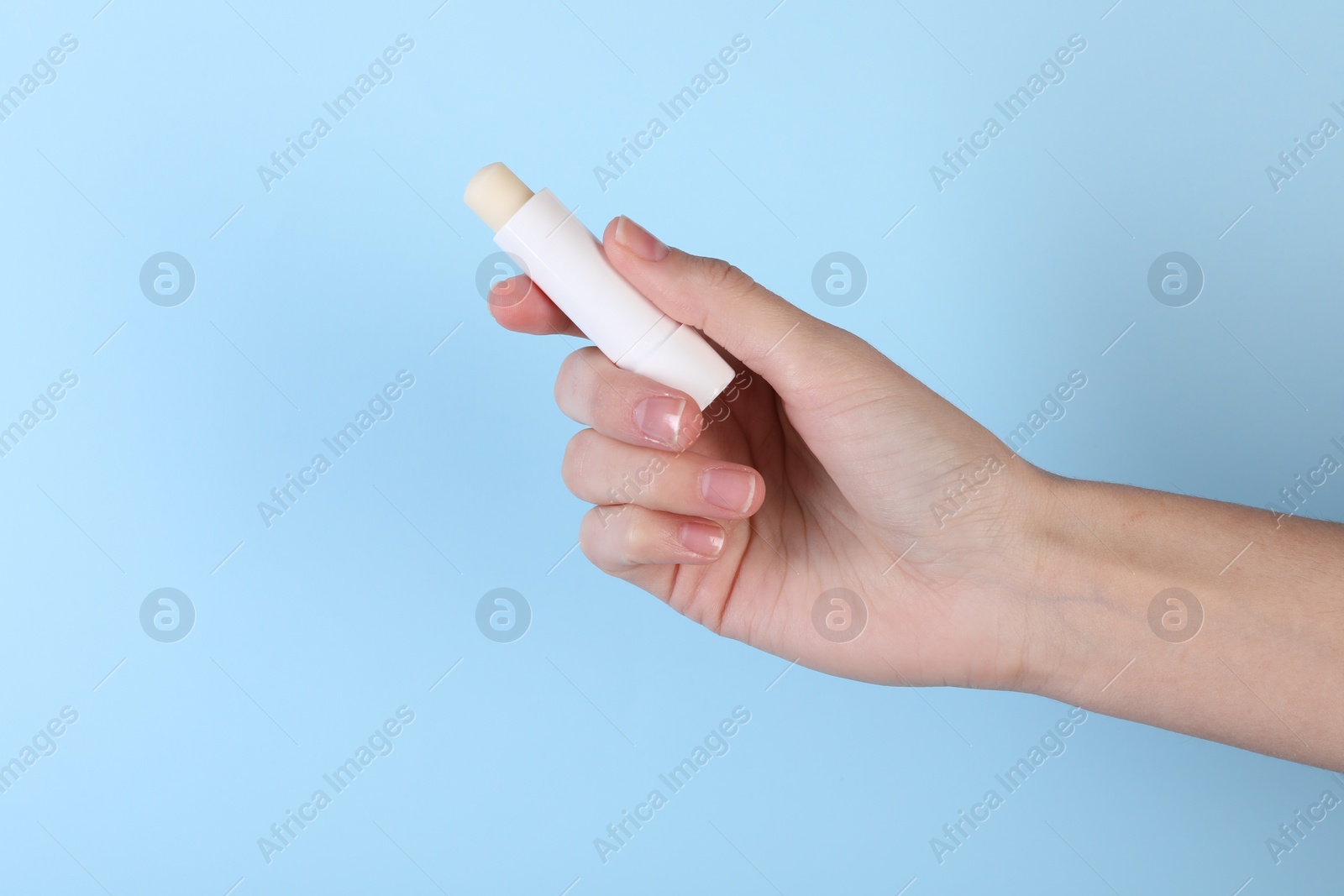 Photo of Woman with lip balm on light blue background, closeup