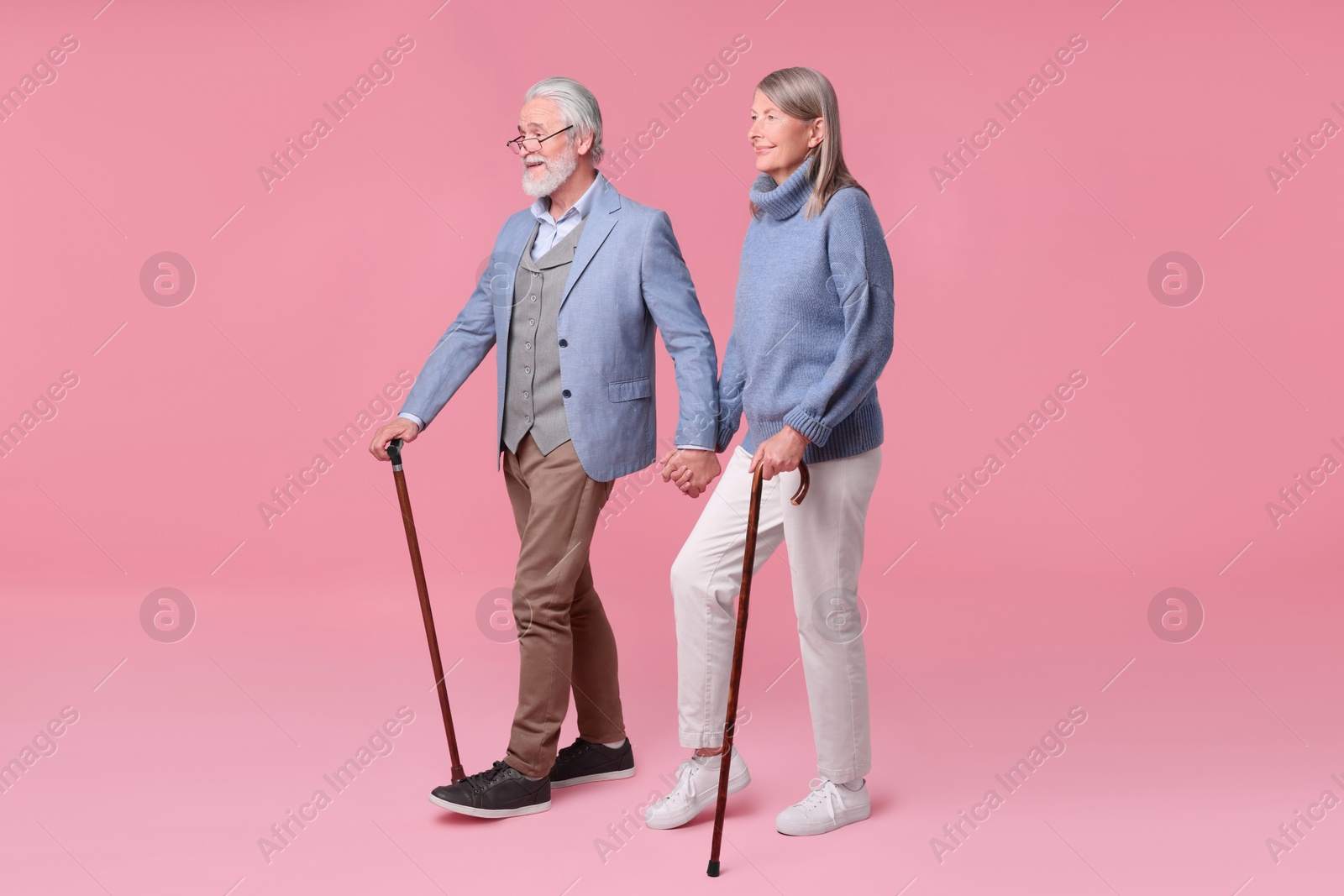 Photo of Senior man and woman with walking canes on pink background