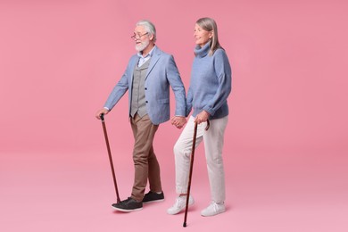 Senior man and woman with walking canes on pink background
