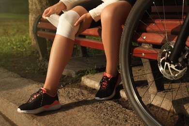 Photo of Young woman applying bandage onto her knee on wooden bench outdoors, closeup