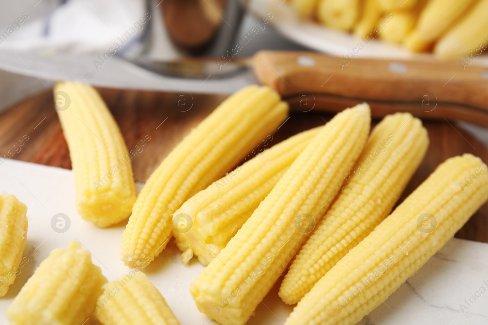 Photo of Tasty fresh yellow baby corns and knife on tray, closeup