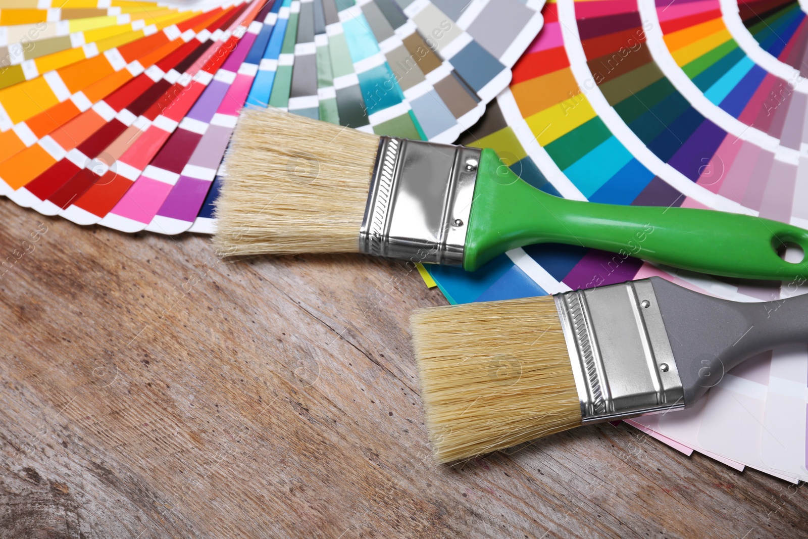 Photo of Paint brushes and color palette samples on wooden background, closeup