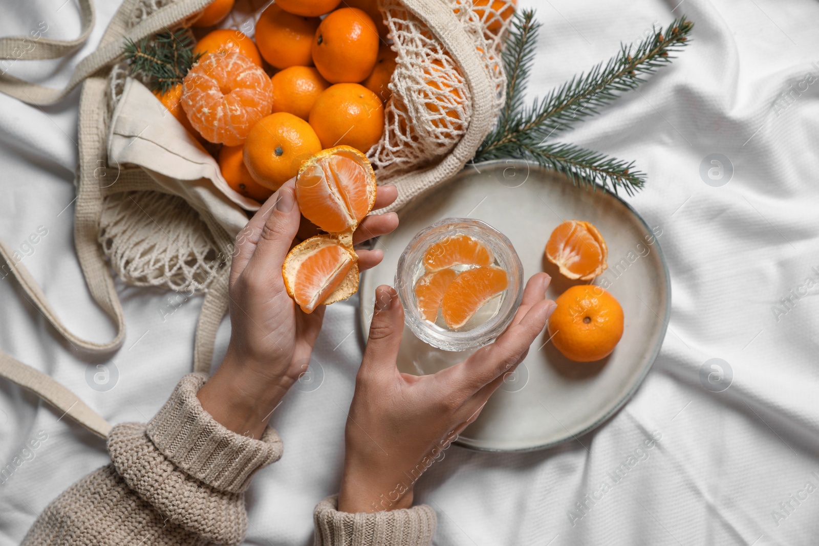 Photo of Woman with delicious ripe tangerines and glass of sparkling wine on white bedsheet, top view