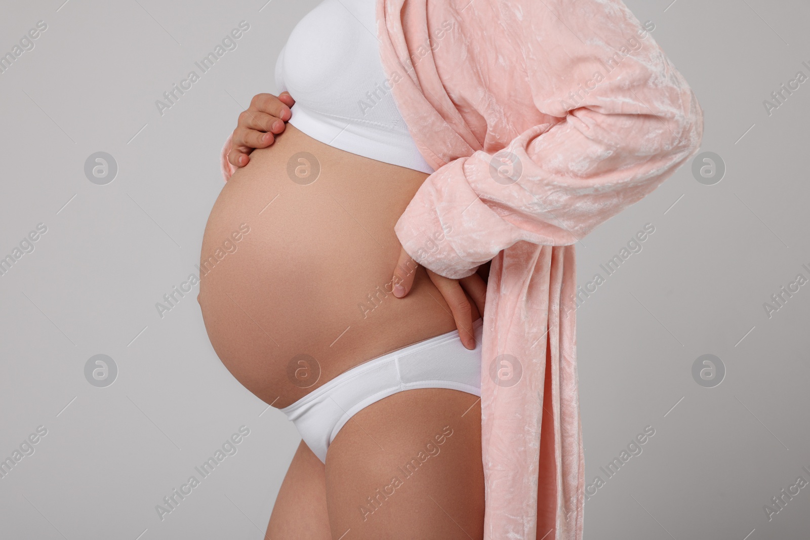 Photo of Pregnant woman in stylish comfortable underwear and robe on grey background, closeup