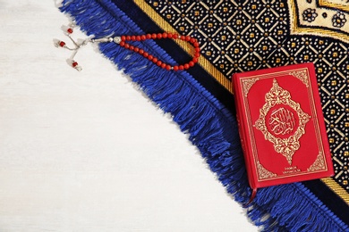 Muslim prayer beads, Quran, rug and space for text on light background, top view