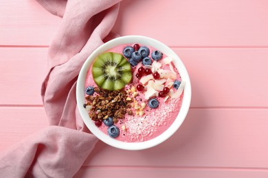 Photo of Tasty smoothie bowl with fresh kiwi fruit, berries and granola on pink wooden table, top view
