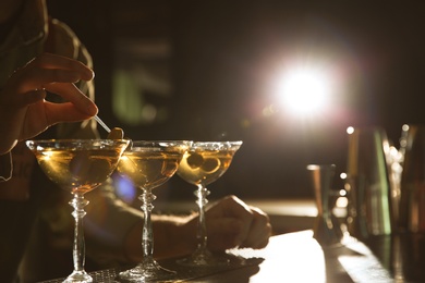 Photo of Barman adding olives to martini cocktail on counter, closeup. Space for text
