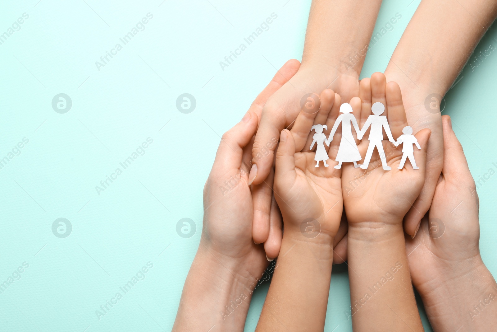 Photo of Parents and child holding paper cutout of family on light blue background, top view. Space for text