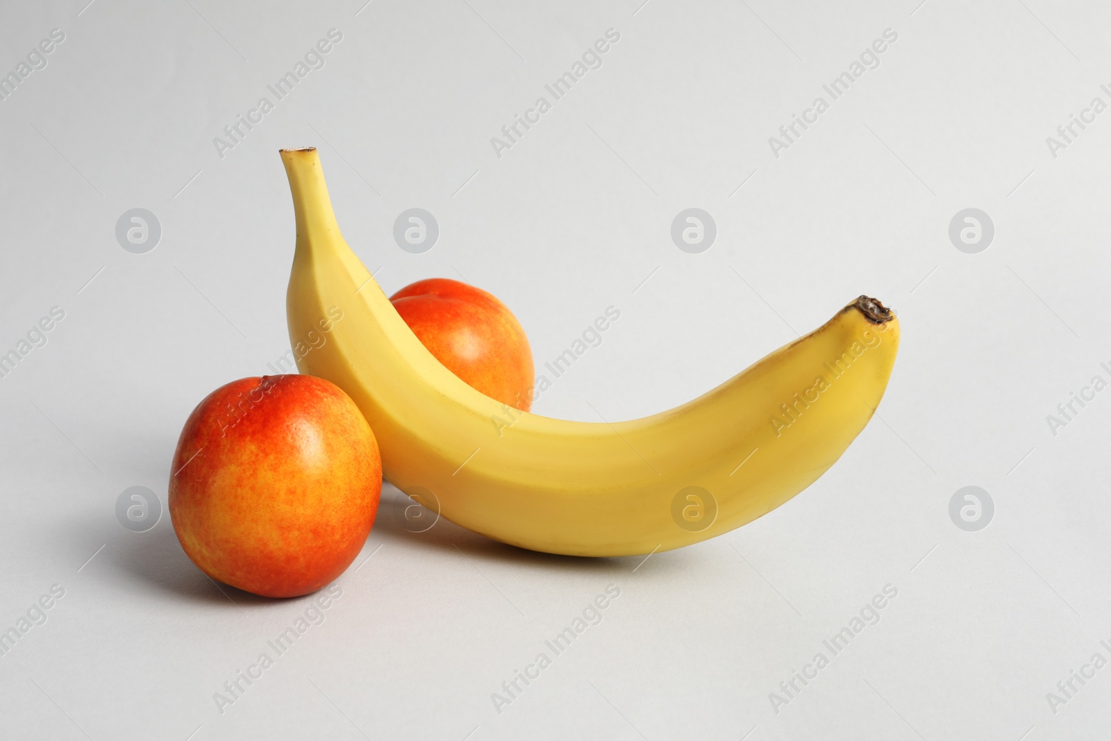 Photo of Banana and nectarines symbolizing male genitals on light grey background. Potency concept