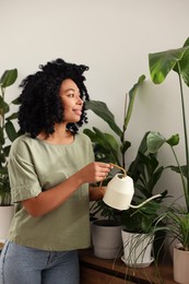 Happy woman watering beautiful potted houseplants indoors