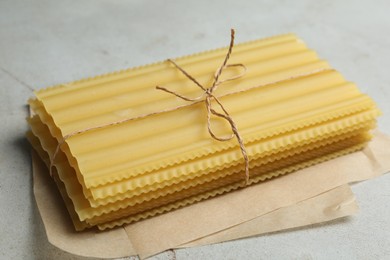 Photo of Uncooked lasagna sheets tied with rope on light grey table, closeup
