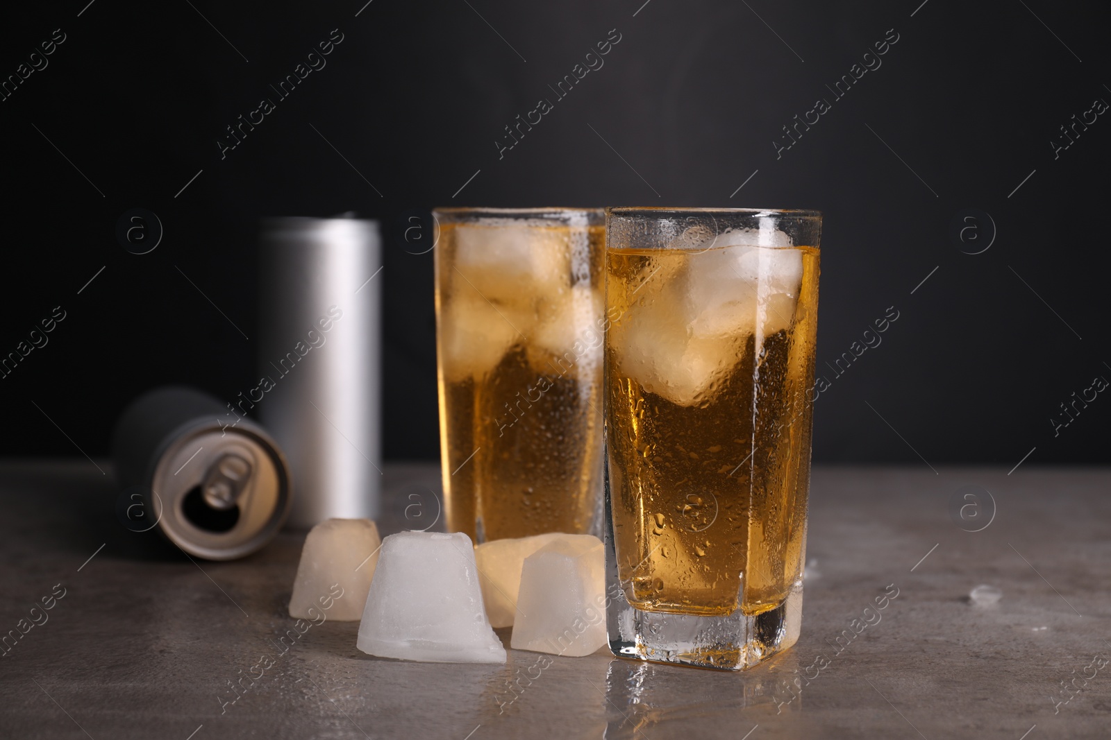 Photo of Tasty energy drink with ice cubes in glasses and aluminium cans on grey table