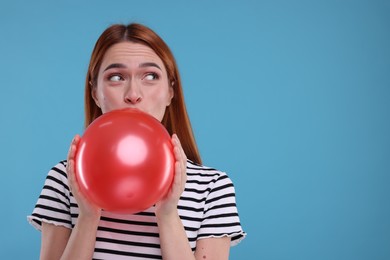 Photo of Woman inflating red balloon on light blue background, space for text