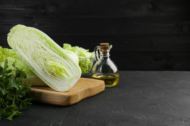 Photo of Fresh Chinese cabbages, parsley and oil on black textured table. Space for text