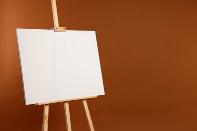 Wooden easel with blank canvas on brown background. Space for text