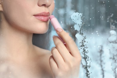 Image of Winter skin care. Closeup of woman applying lip balm. Beautiful forest on background