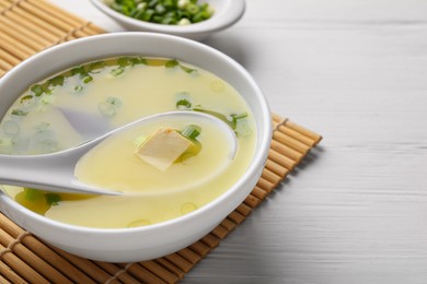 Photo of Bowl of delicious miso soup with tofu and spoon served on white wooden table, closeup. Space for text