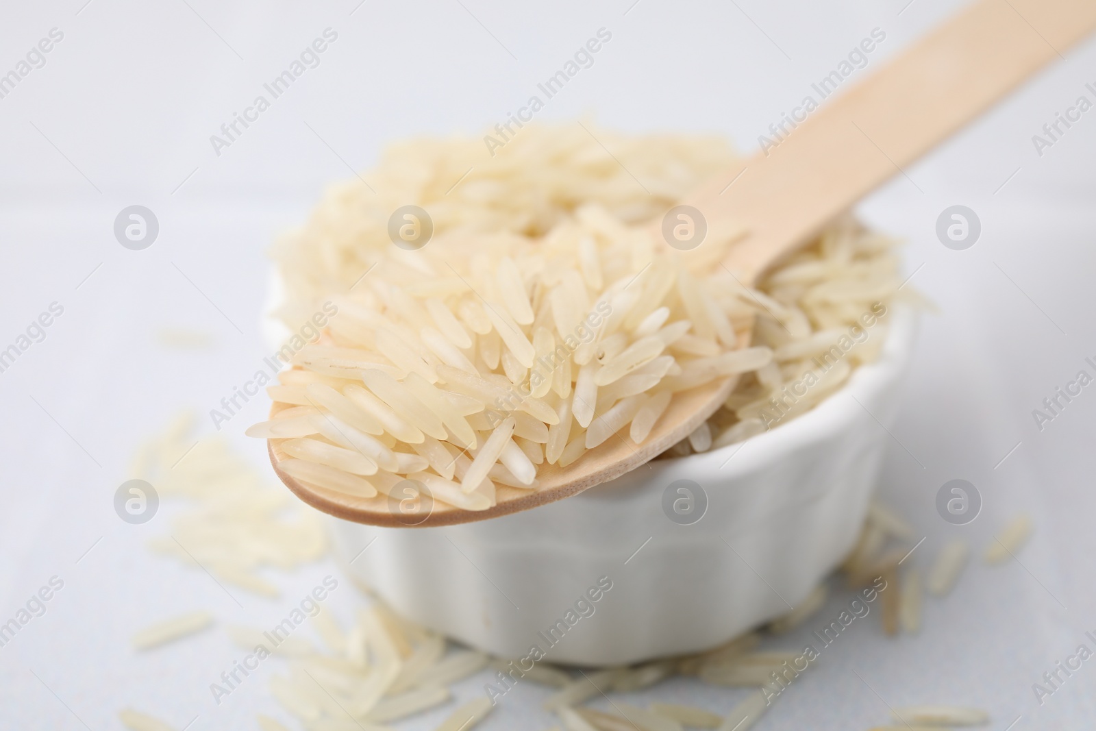 Photo of Wooden spoon and bowl with raw rice on white table, closeup