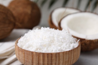 Coconut flakes in bowl and nuts on table, closeup