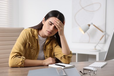 Photo of Young woman suffering from headache at wooden table in office