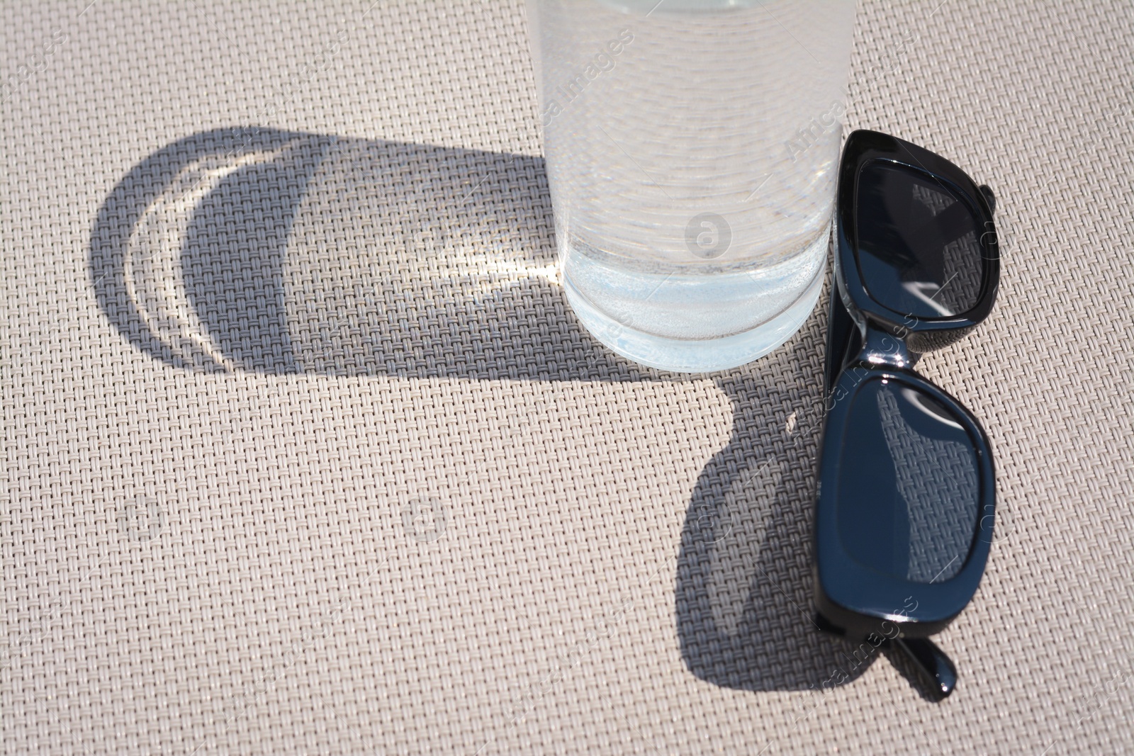 Photo of Stylish sunglasses and glass of water on grey surface, closeup. Space for text