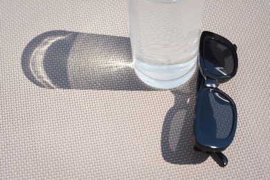 Stylish sunglasses and glass of water on grey surface, closeup. Space for text