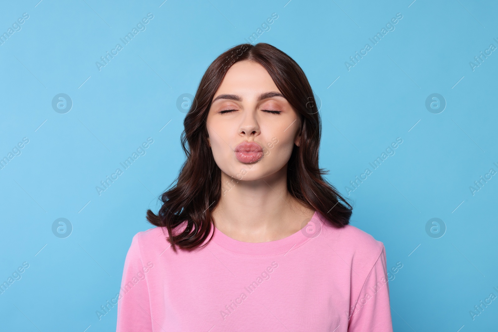 Photo of Beautiful young woman giving kiss on light blue background