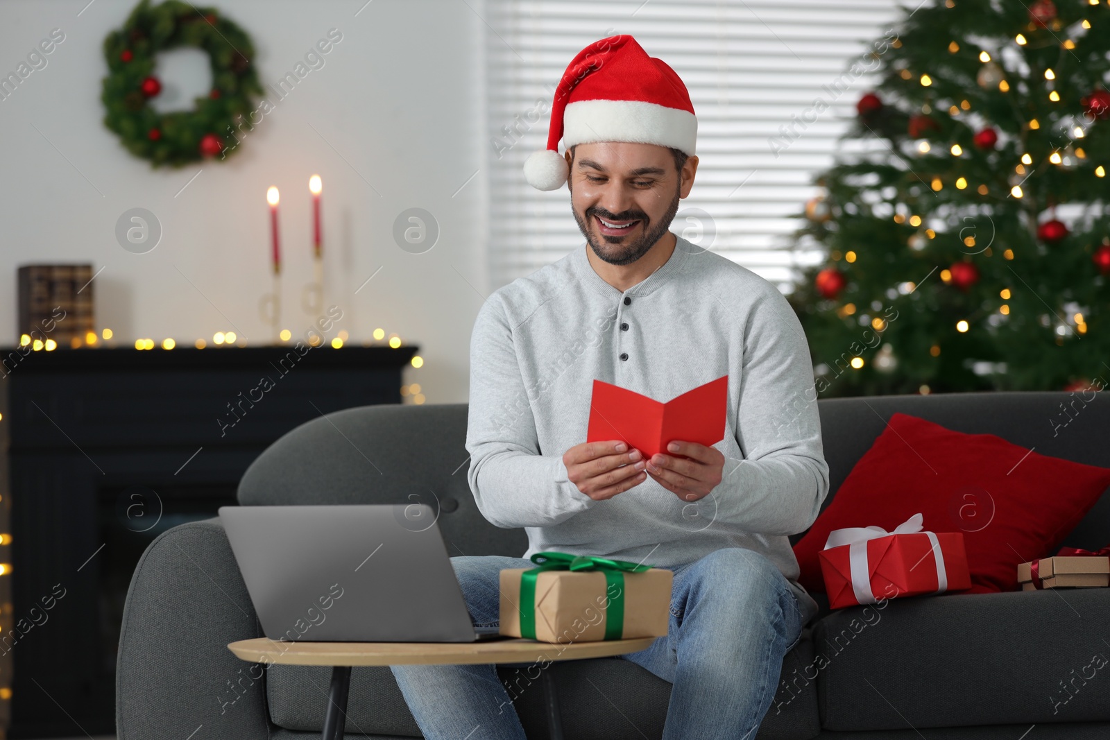 Photo of Celebrating Christmas online with exchanged by mail presents. Man reading greeting card during video call on laptop at home