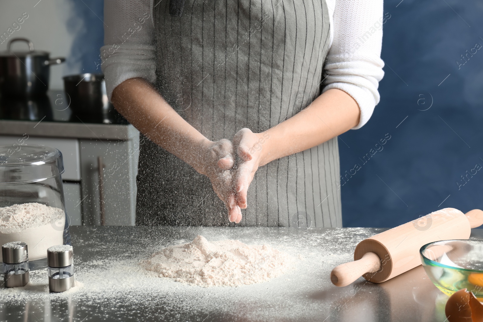 Photo of Woman sprinkling flour over table in kitchen