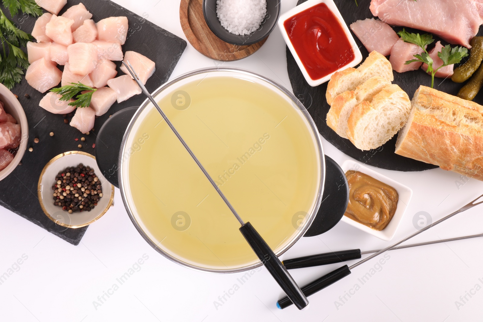 Photo of Oil in fondue pot, forks, sauces, pieces of raw meat and other products on white background, flat lay