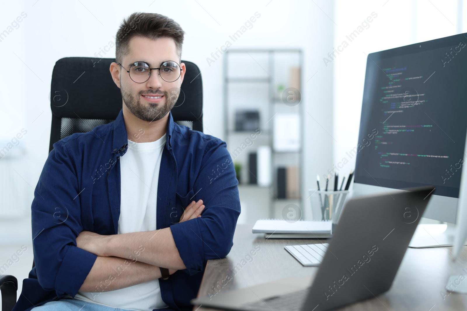 Photo of Happy young programmer working with laptop in office