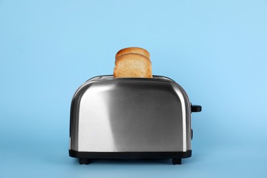 Photo of Electric toaster with bread slices on light blue background