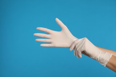 Doctor wearing medical gloves on light blue background, closeup