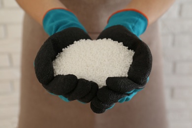 Photo of Woman holding pile of granular mineral fertilizer on blurred background, closeup