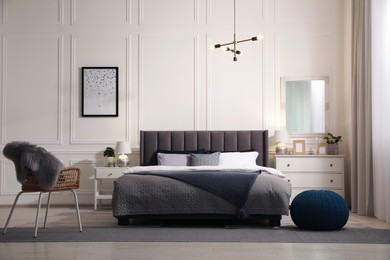 Stylish bedroom interior with large comfortable bed, chair and chest of drawers