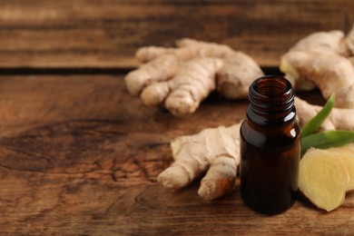 Glass bottle of essential oil and ginger root on wooden table, space for text