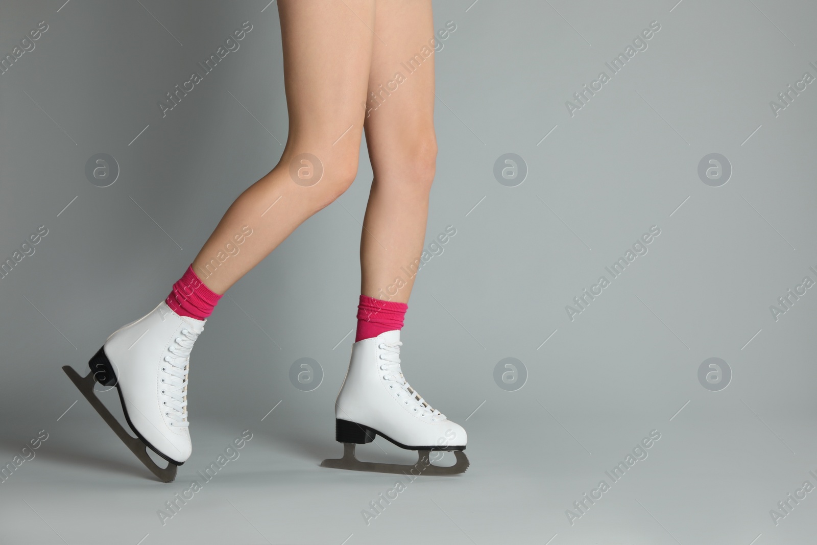 Photo of Woman in elegant white ice skates on grey background, closeup of legs. Space for text