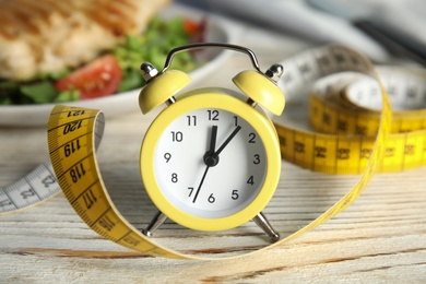 Alarm clock and measuring tape on white wooden table. Diet regime