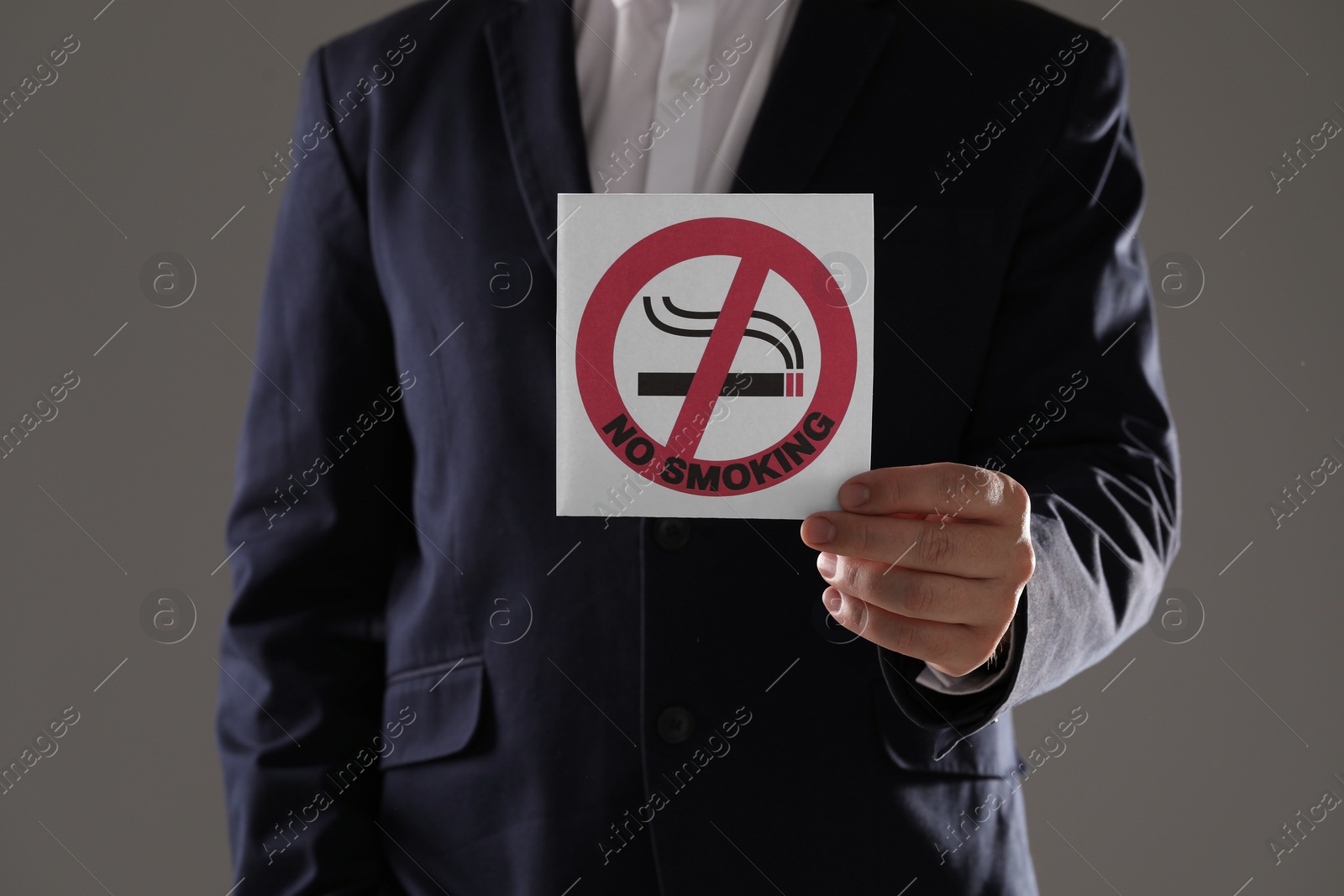 Photo of Man holding card with no smoking sign on gray background, closeup