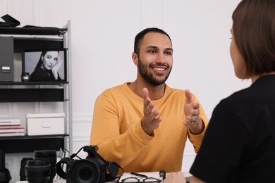 Photo of Young professional photographer with camera talking with woman in modern photo studio