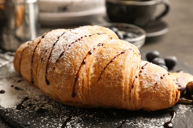 Photo of Tasty croissant with sugar powder on slate plate, closeup