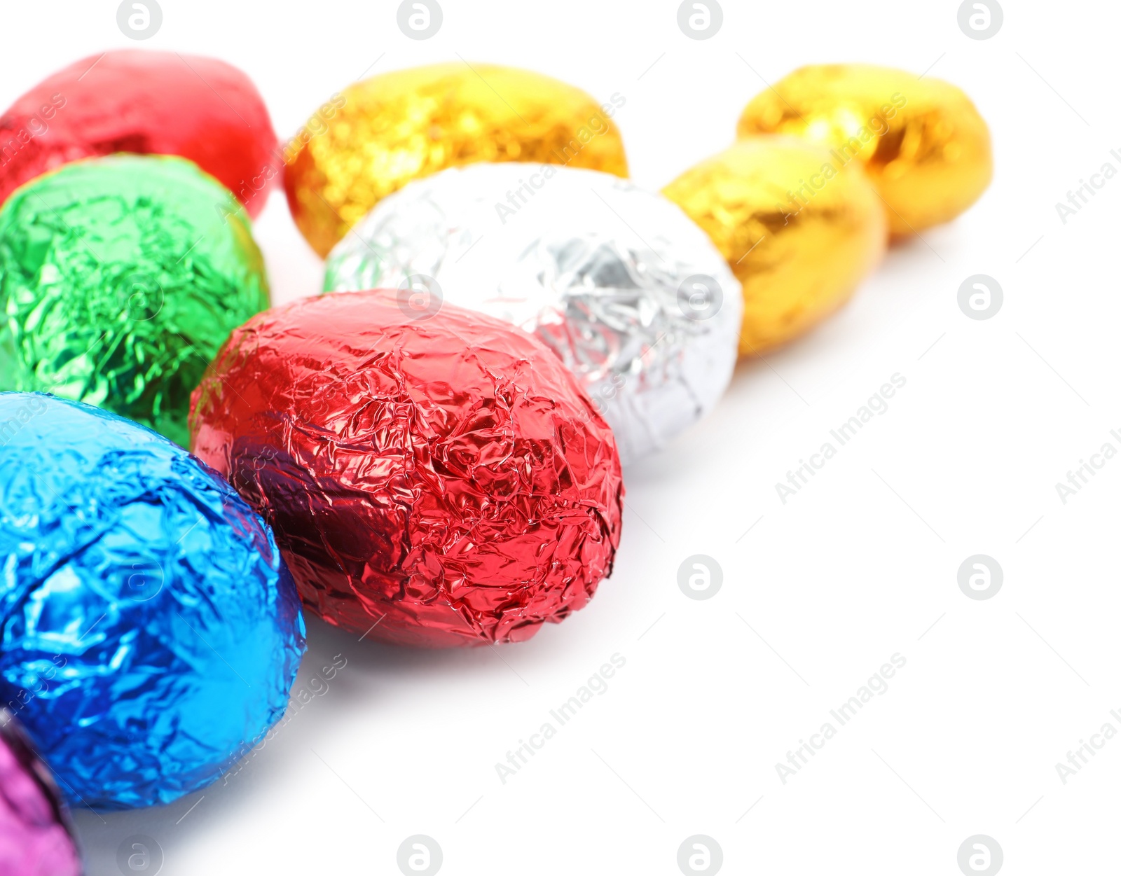 Photo of Many chocolate eggs wrapped in bright foil on white background, closeup